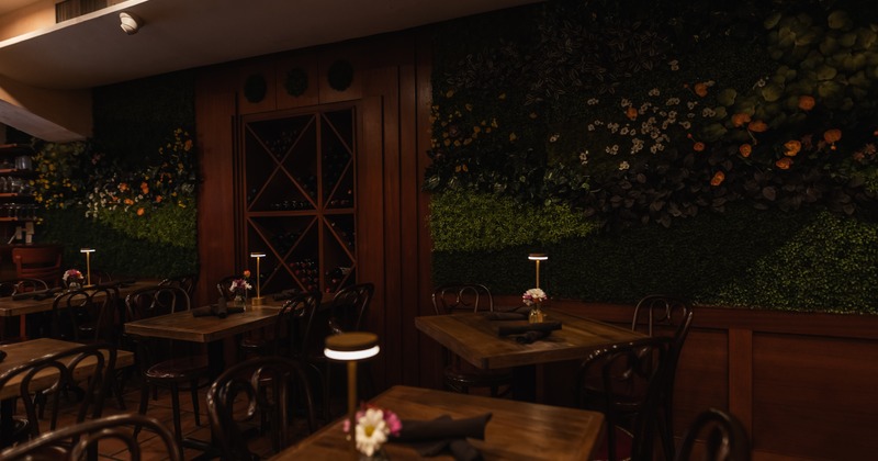Restaurant interior with a green floral wall, wooden tables, and warm lighting