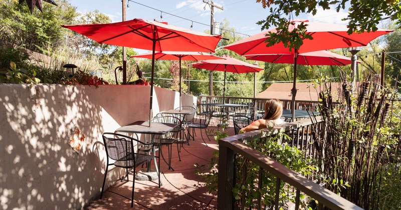 Outdoor patio with red umbrellas over tables, surrounded by greenery and decorative walls