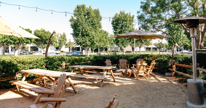 Exterior, a hedge, wooden tables with benches, large wooden chairs, space heater