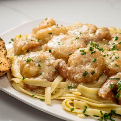 A plate of fettuccine pasta topped with creamy garlic shrimp sprinkled with chives.