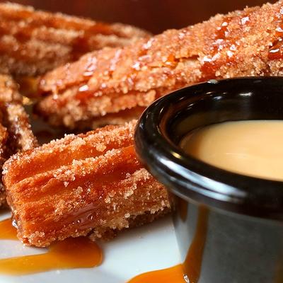 Cinnamon sugar churros with caramel drizzle and a cup of sweet sauce.