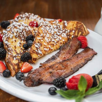 French toast with berries, powdered sugar, and crispy bacon.