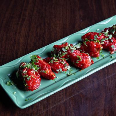 Marinated chicken pieces dipped in a special sauce served on a green platter.