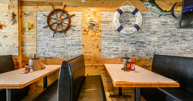 Interior - wooden walls with handwritten notes, a ship's wheel, a lifebuoy, black leather booths