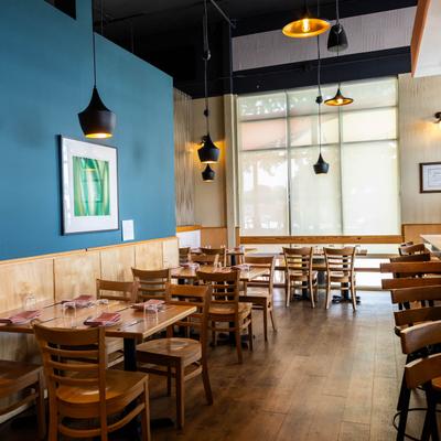 Bright modern dining room with wooden tables, pendant lights, and teal accent wall.