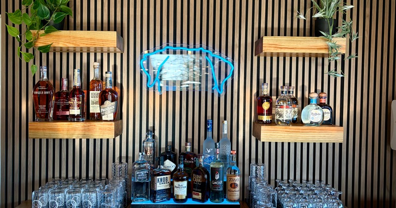 Bar shelves displaying liquor bottles with a blue neon sign above them