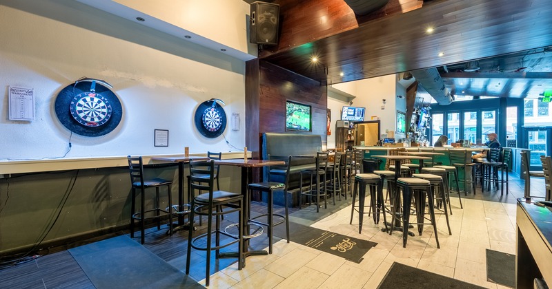 Interior of a sports bar with bar stools and high tables and two electronic dartboards on the wall