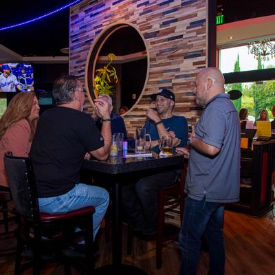 In a lively bar setting, four people chat, and laugh around a high-top table.