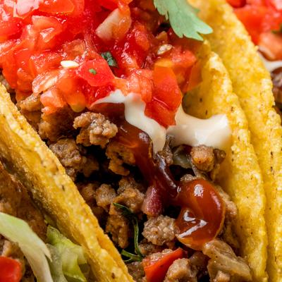 Taco filled with ground beef, topped with salsa and sauces, close-up.