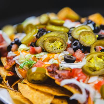 Loaded nachos featuring melted cheese, jalapenos, black olives and tomatoes, close-up.