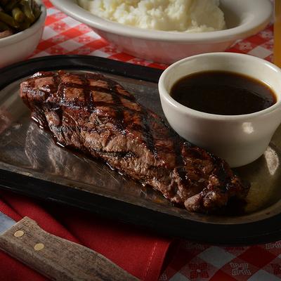 Grilled steak served on a sizzling metal platter with a side of dark dipping sauce.