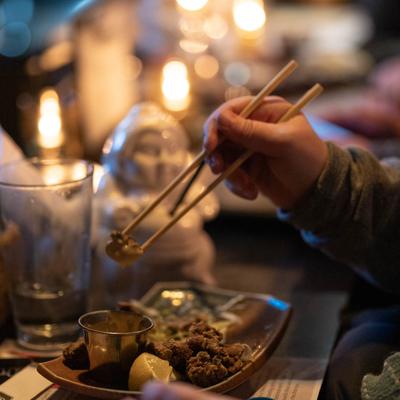 Hand holding a bite of food with chopsticks, above the plate on the candle lit table.