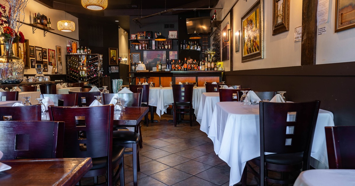 Warmly lit interior - white-tableclothed tables, dark wood chairs, wall art, a stocked bar.
