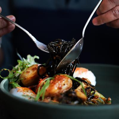 A person twirling dark noodles over a plate of seafood.