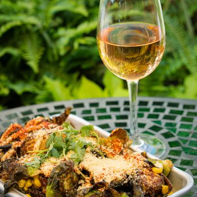 Elote Brussels sprouts served in a white metal tray beside a glass of wine.