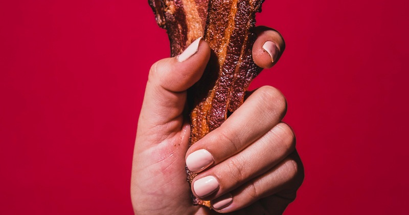 Hand holding smoked bacon against velvet red background