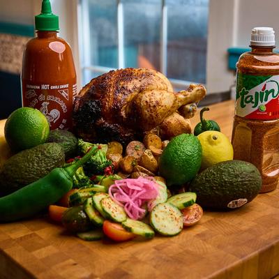 A wooden cutting board with a roasted whole chicken and vegetable arrangement.