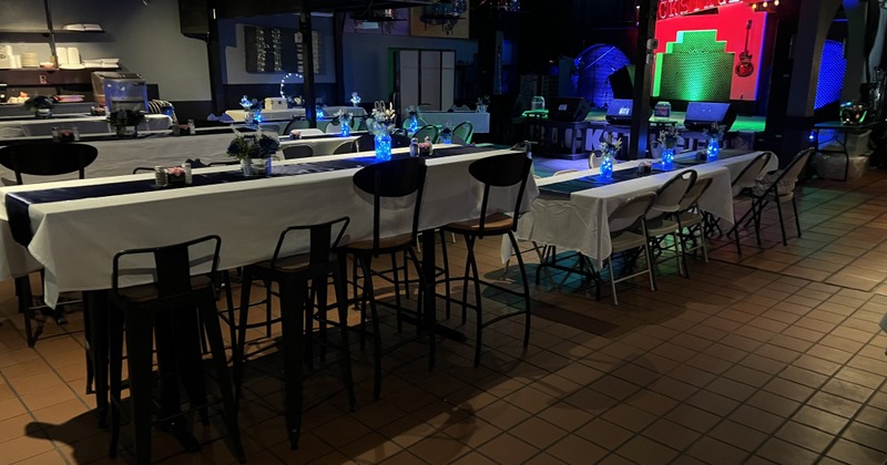 Dimly lit venue with long tables decorated with white cloths and blue glowing centerpieces