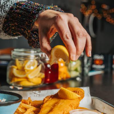 A hand squeezing a lemon over a plate of fish and chips.