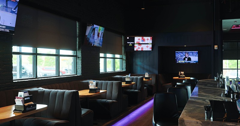 Interior of a modern sports bar with booths, a bar counter and multiple flat-screen televisions.