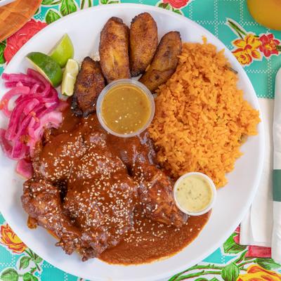 Chicken Mole served with rice, fried plantains, pickled red onions and sauces.