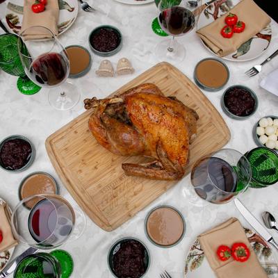 Roasted turkey on a wooden cutting board, surrounded by wine, side dishes, and dinnerware.