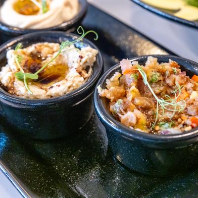 Two black bowls on a glossy black tray hold colorful dips garnished with fresh green.