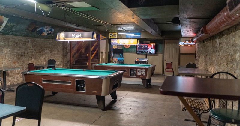 A room with two pool tables, stone walls, and beer advertisements, including neon signs