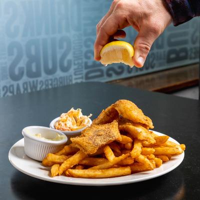 A hand squeezes lemon on fried cod on a plate with fries and sides.