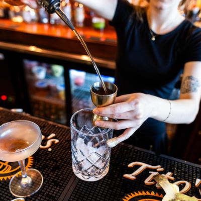 A bartender pouring a beverage into a jigger over a cocktail glass filled with ice.