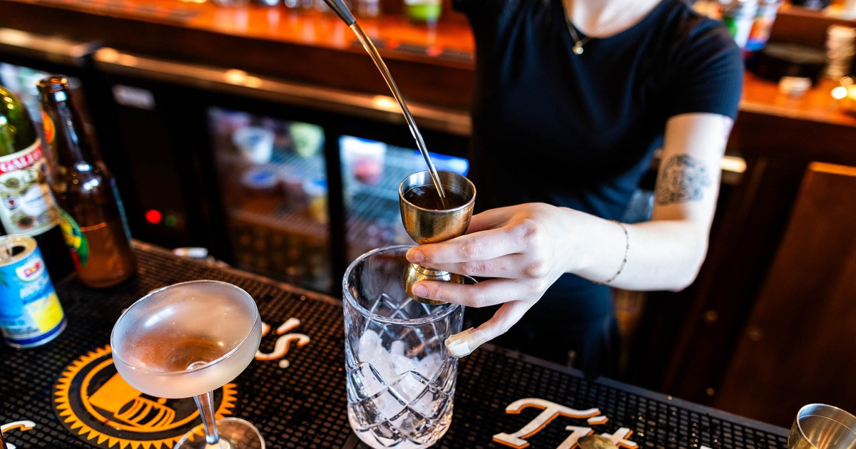 A bartender pouring a beverage into a jigger over a cocktail glass filled with ice