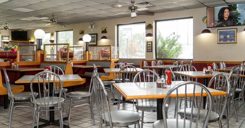 Interior -tables, metallic chairs, booths with flower decorations and a TV on the wall.