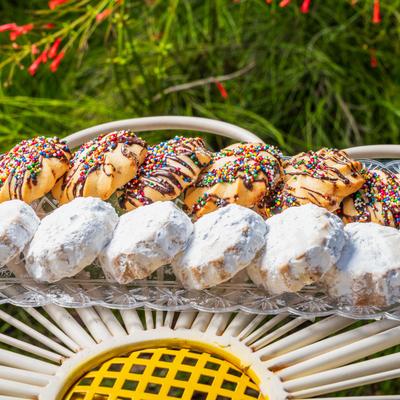 Colorful sprinkle cookies and powdered sugar cookies arranged on a clear tray outdoors.
