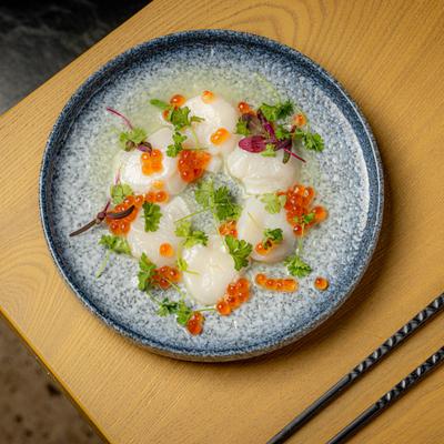 Scallop Crudo garnished with salmon roe and fresh herbs.