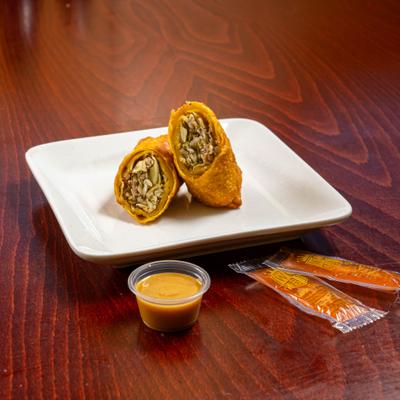 Egg roll halves on a plate with dipping sauce and sauce packets on the table.