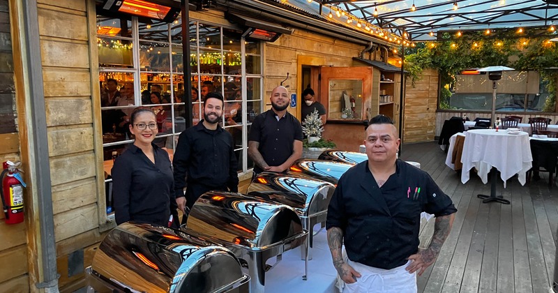 Catering staff posing beside chafing dishes in an outdoor event space