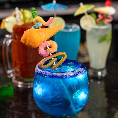 Blue Margarita garnished with a whimsical candy skewer and other cockatils in the background.