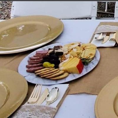 A  table setting with a charcuterie board, gold rimmed plates and cutlery.
