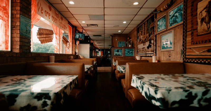 Restaurant interior with brown booths, cow-print tables, Western decor, and a red banner