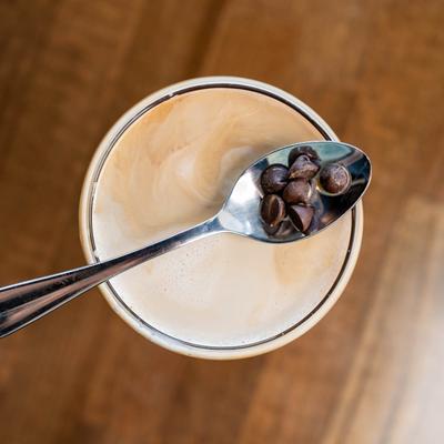 Espresso martini glass sits on a wooden table, topped with a spoon holding chocolate chips.
