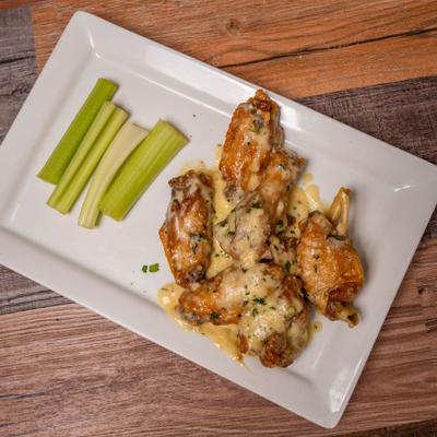 Crispy chicken wings with creamy cheese sauce and celery sticks on a white plate.