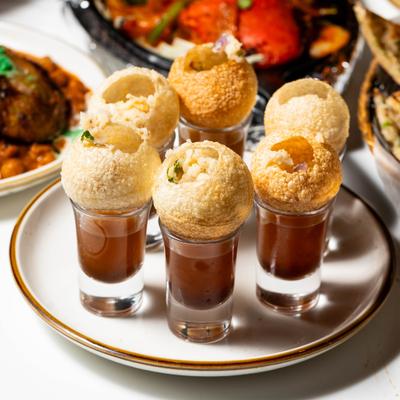 Puri shells served on top of shot glasses filled with tangy, flavored water.
