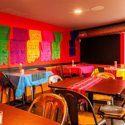 Mexican restaurant interior with wooden tables, colorful tablecloths, and papel picado decorations.