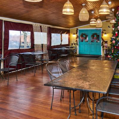 Enclosed patio with black metal tables, woven pendant lights, and a Christmas tree.
