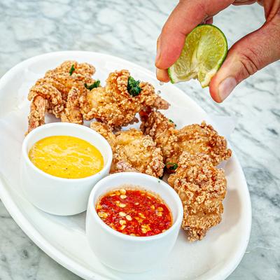 Deep fried shrimp and dips, hand squeezing lime wedge over the dish