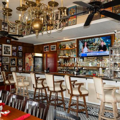 Bar area with white stools, liquor bottles, wall art, and chandeliers.