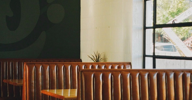 Café interior - brown leather booths, wooden tables, turquoise pendant lights, large window