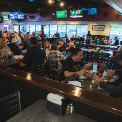 Dining area with multiple television screens and people seated at tables with food and drinks.