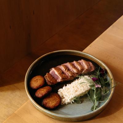 Sliced duck breast with rice, potato rounds, and greens on a ceramic plate.