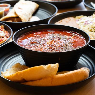Menudo bowl and toast on a table with assorted dishes.